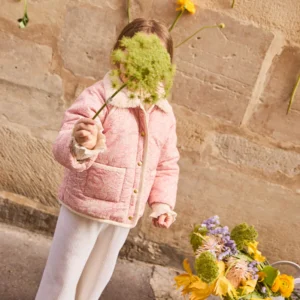 Meisje plukt bloemen bij muur.